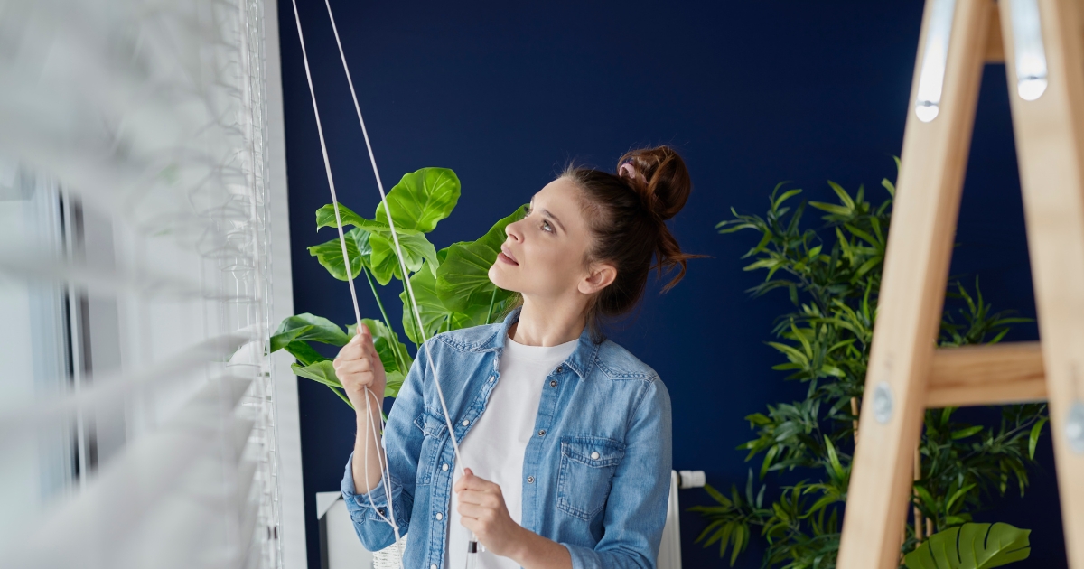 a woman pulling the strings of the blinds