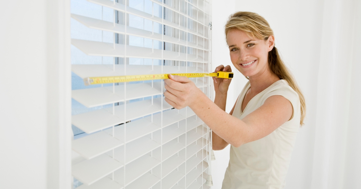 a smiling woman measuring the blinds